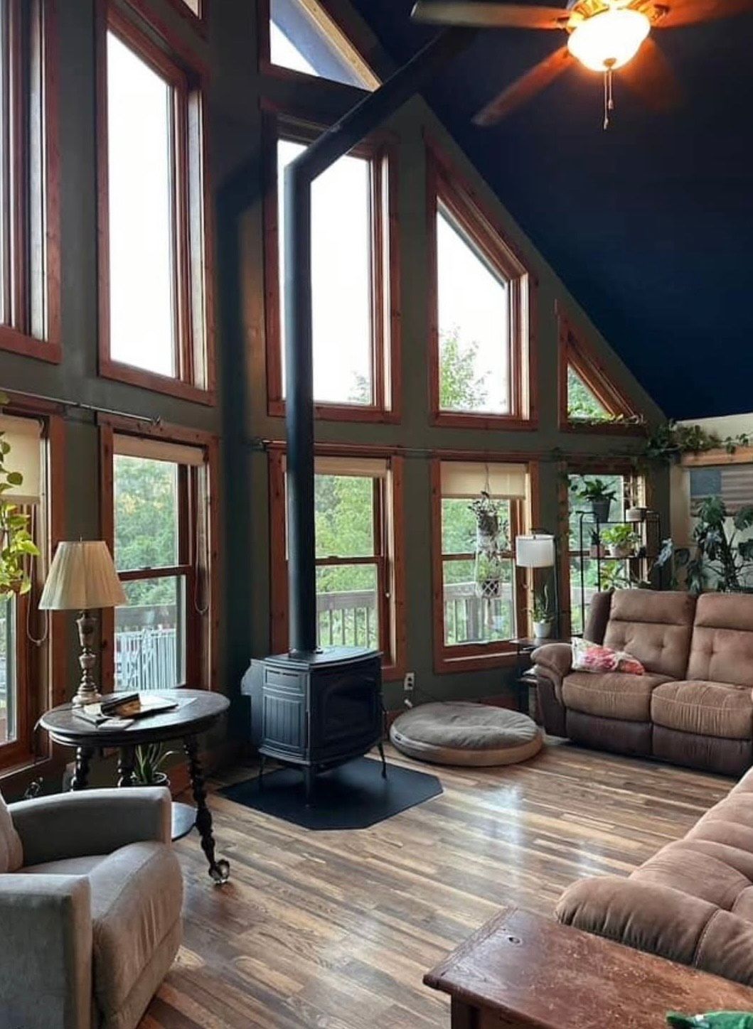 Living room with wood stove, tall windows, brown furniture, and a dark blue ceiling.