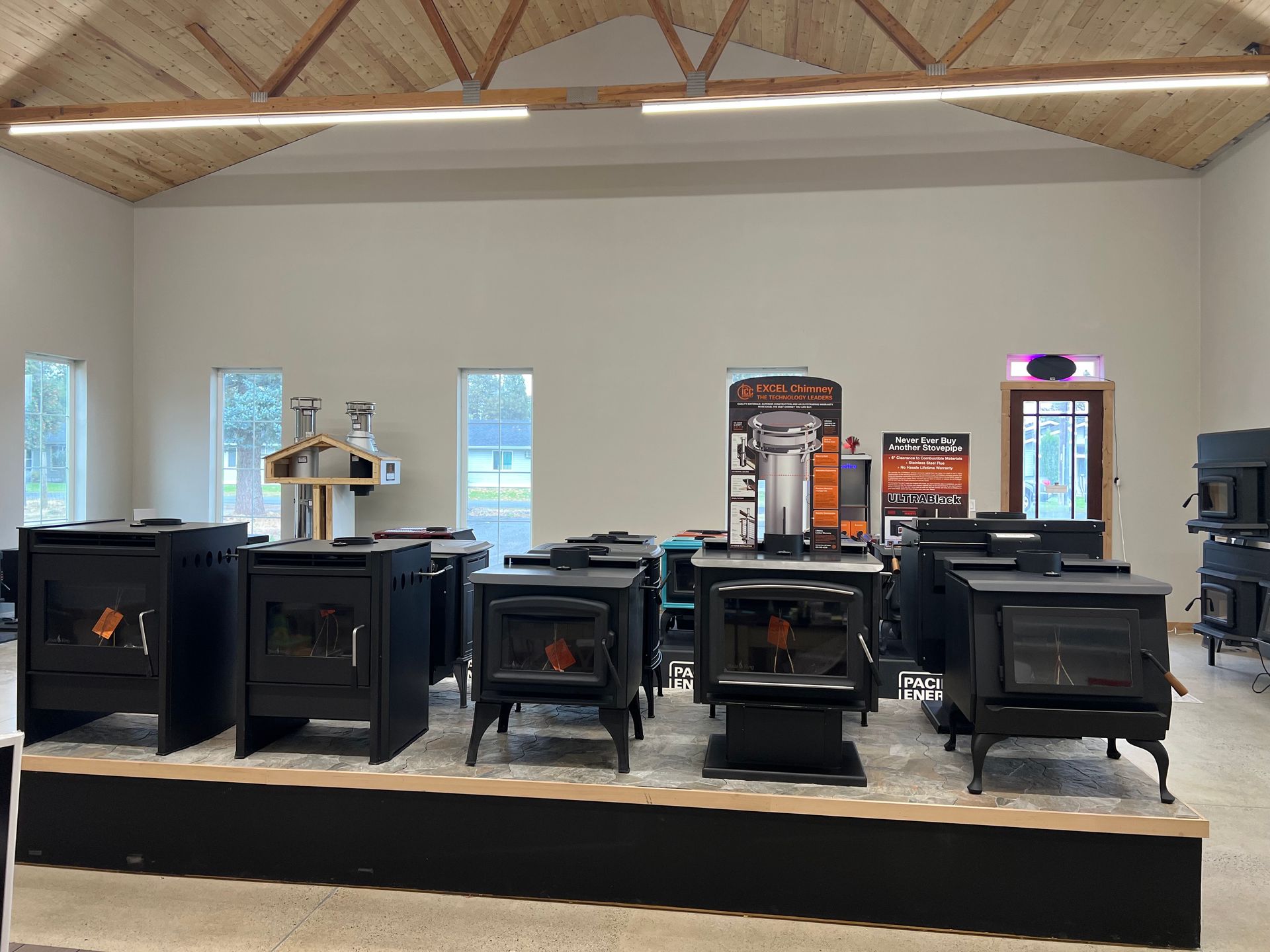 Wood-burning stoves on display in a showroom. Black metal stoves sit on a raised platform, under neutral lighting.