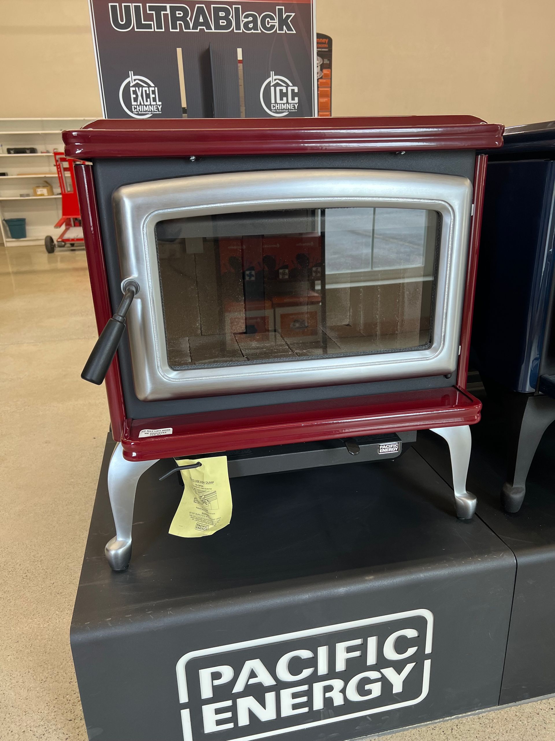 Red and silver wood-burning stove with a large glass door, on display at a store, labeled