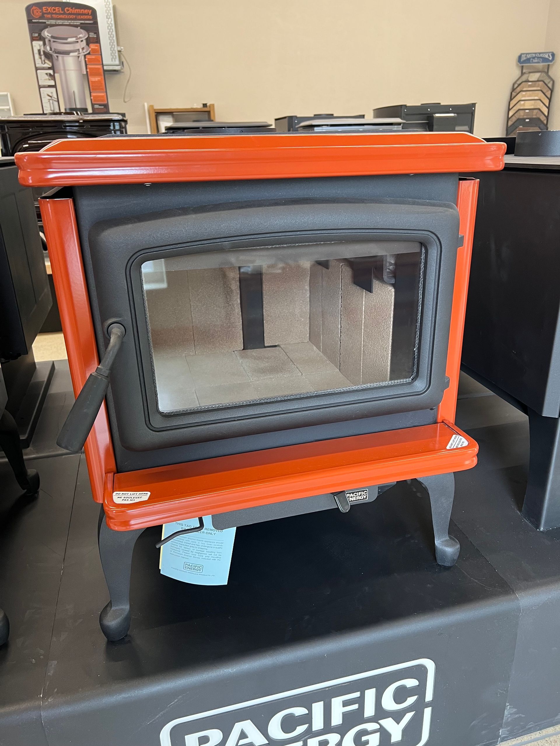 Orange and black wood-burning stove with a glass door, sitting on a black display platform.