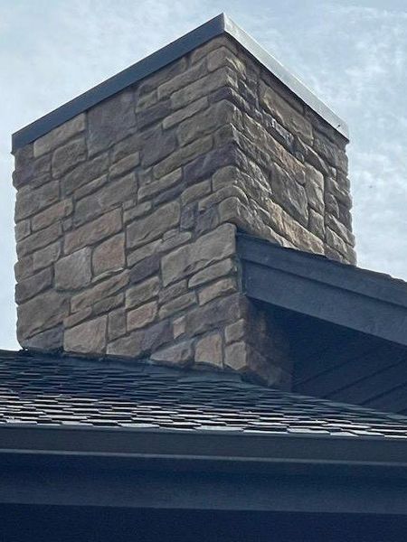 Stone chimney extending from a dark roof against a cloudy sky.