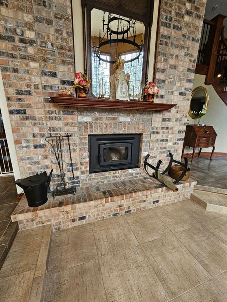 Brick fireplace with a black insert, wooden mantel, and brick hearth, with a mirror and decor.