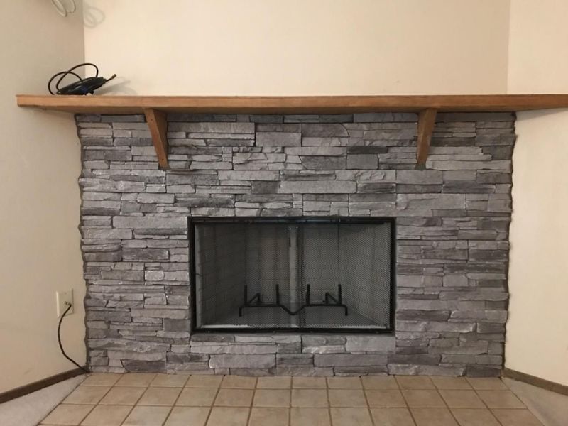 Fireplace with gray stone facing, wooden mantel, and a black glass screen.