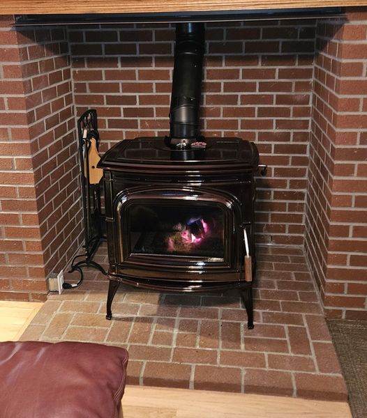 A wood-burning stove inside a brick fireplace. Flames glow through the glass door.
