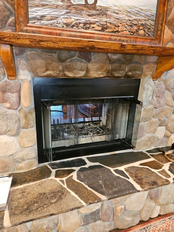 Fireplace with stone surround, a black metal firebox and glass doors. A painting hangs above.