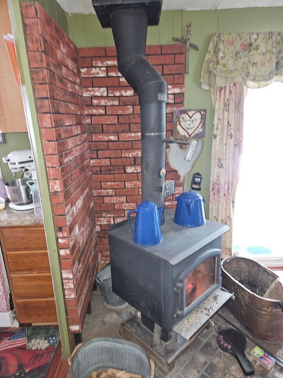 Wood-burning stove with a brick backing in a kitchen. Two blue items sit on the stove top.