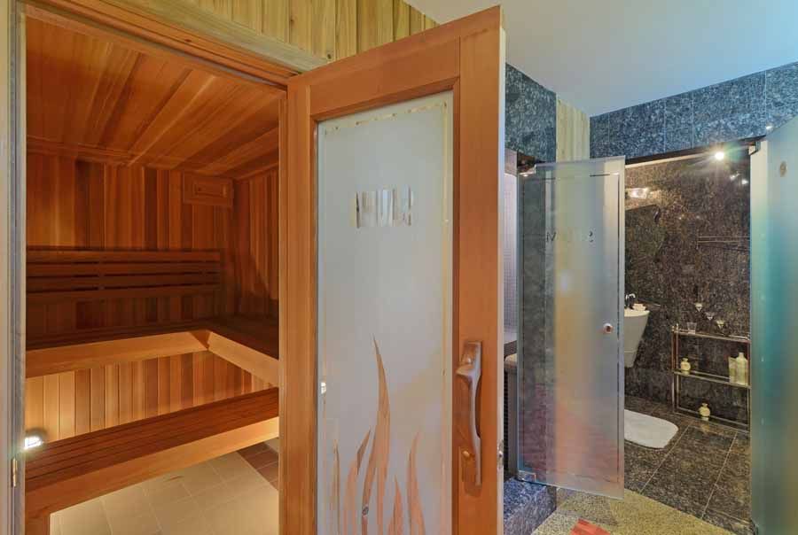 A wooden sauna with a glass door leading to a bathroom.