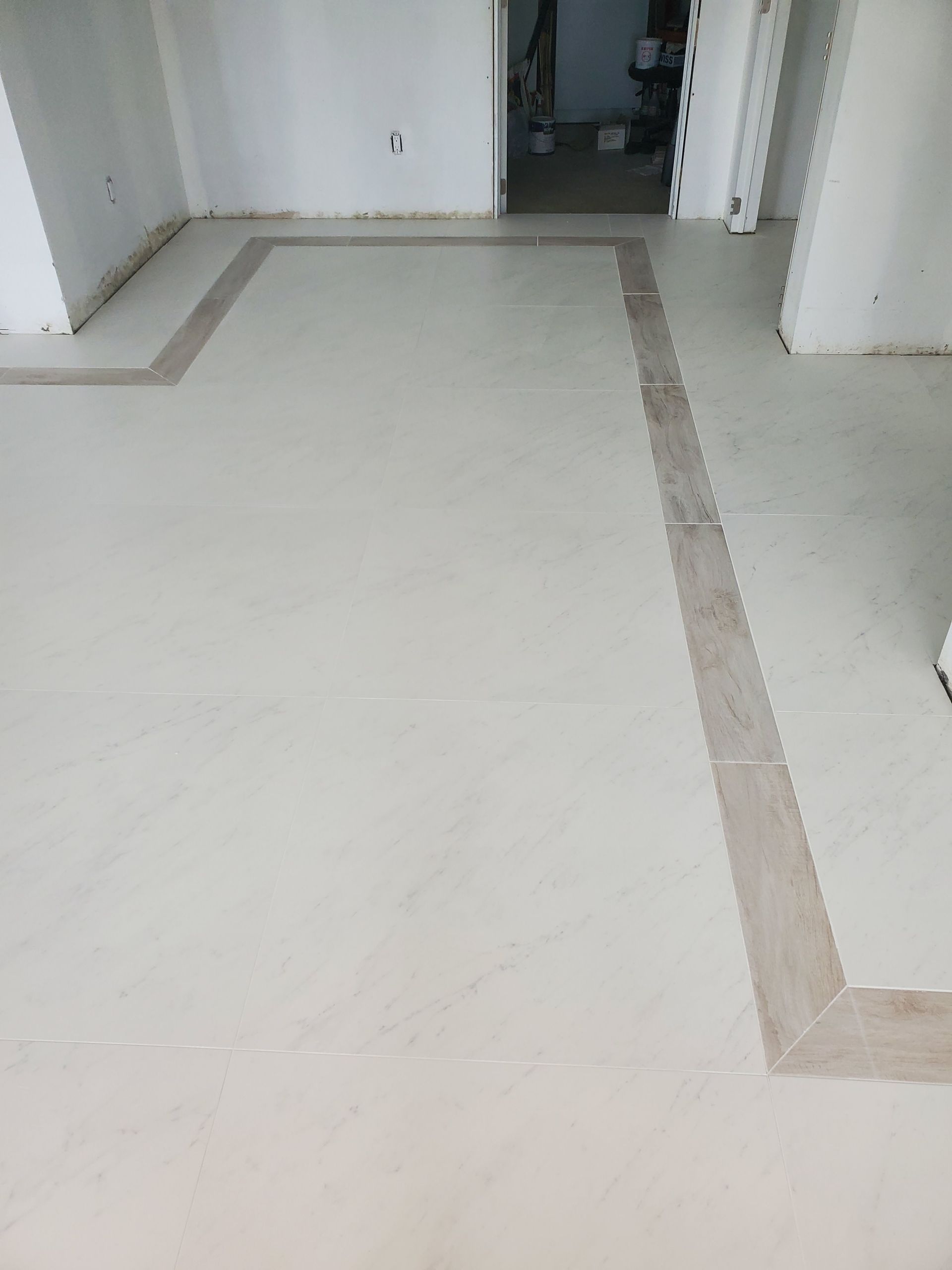 A white tile floor with a brown border in a room.