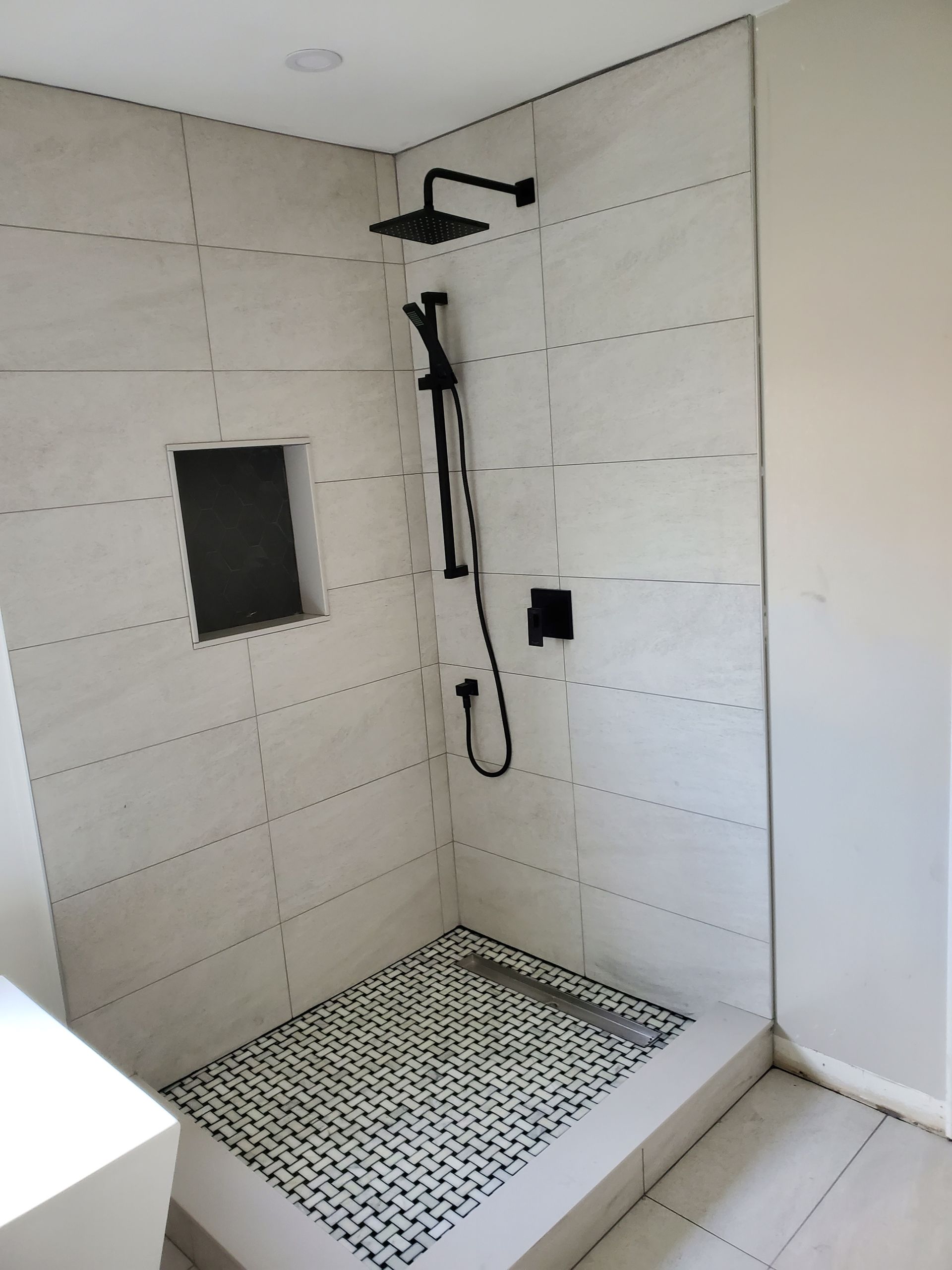 A bathroom with a walk in shower with a black shower head