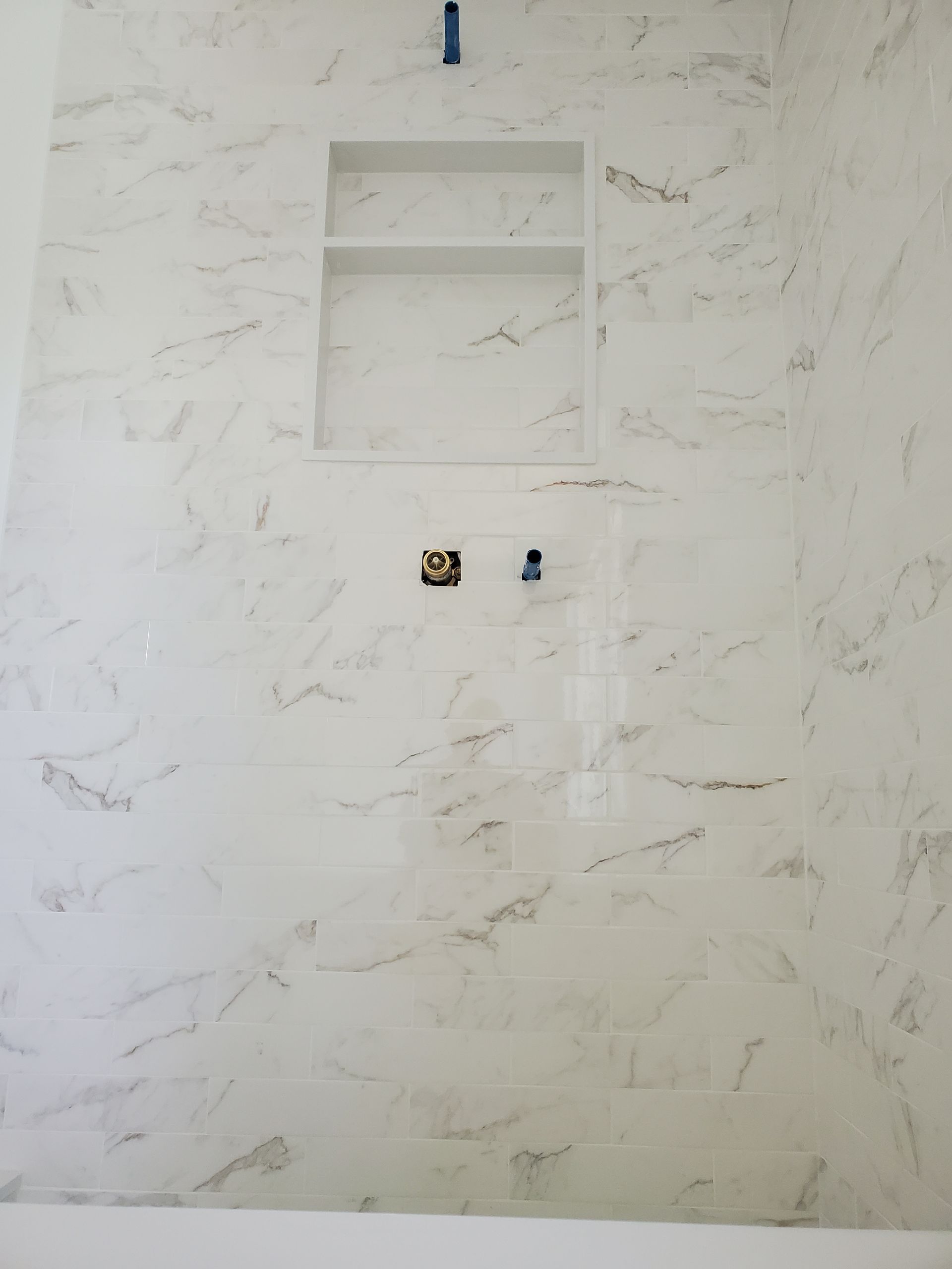 A bathroom with a marble shower wall and a soap dish.