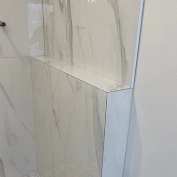 A bathroom with marble tiles on the wall and a shelf in the shower.