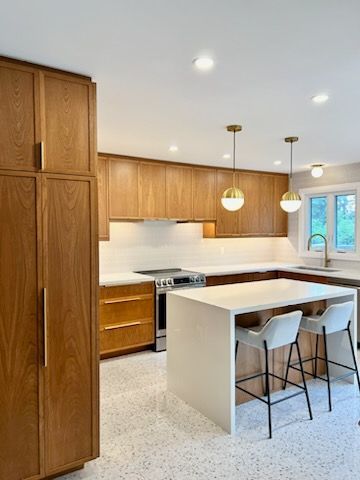 A kitchen with wooden cabinets , a large island , stools , a refrigerator and a stove.