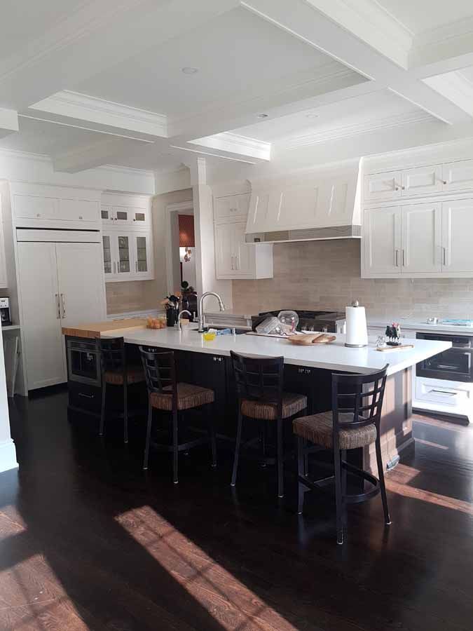 A kitchen with white cabinets , a large island , stools and a stove.