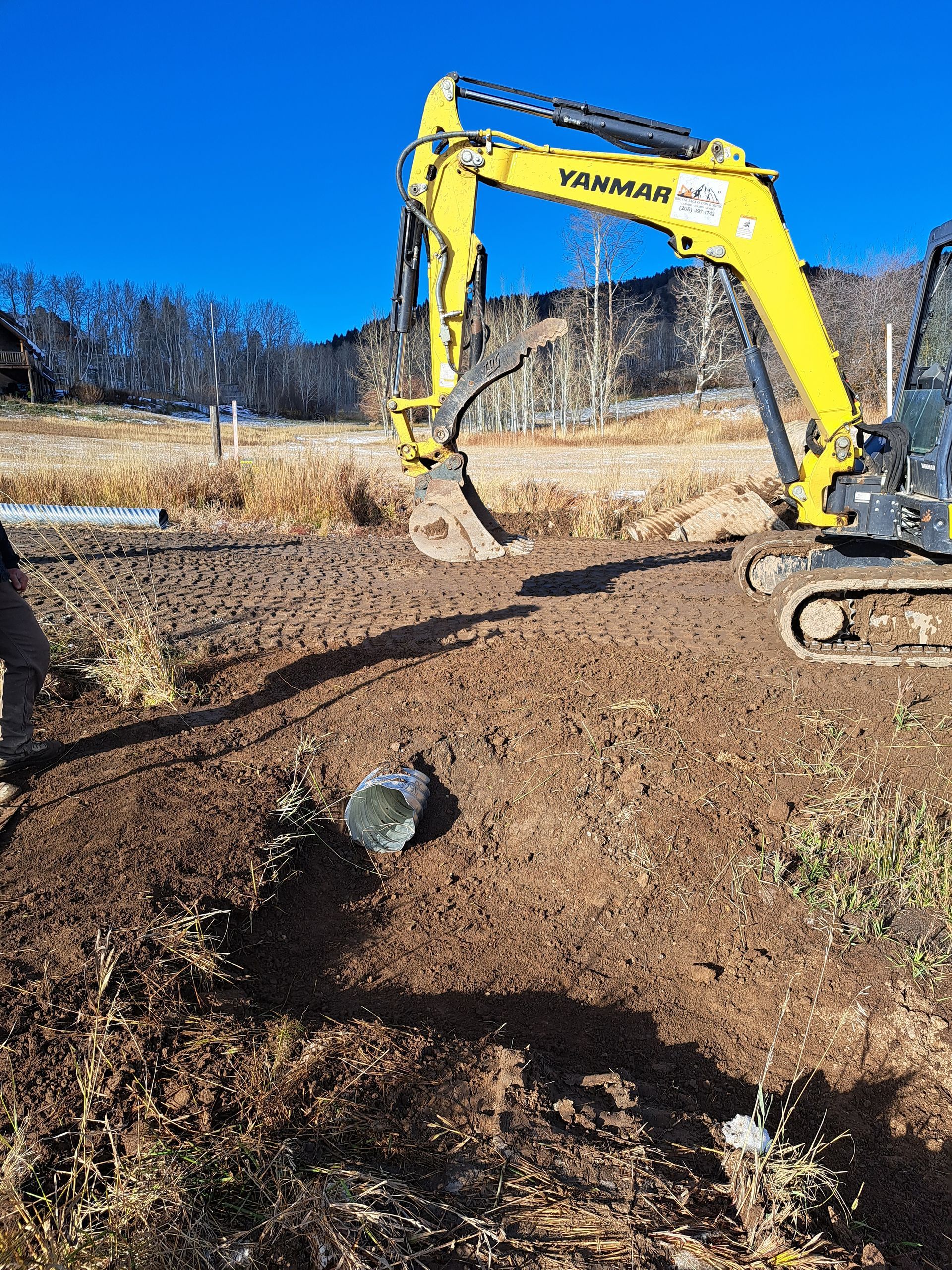 A yellow excavator is digging a hole in a dirt field.