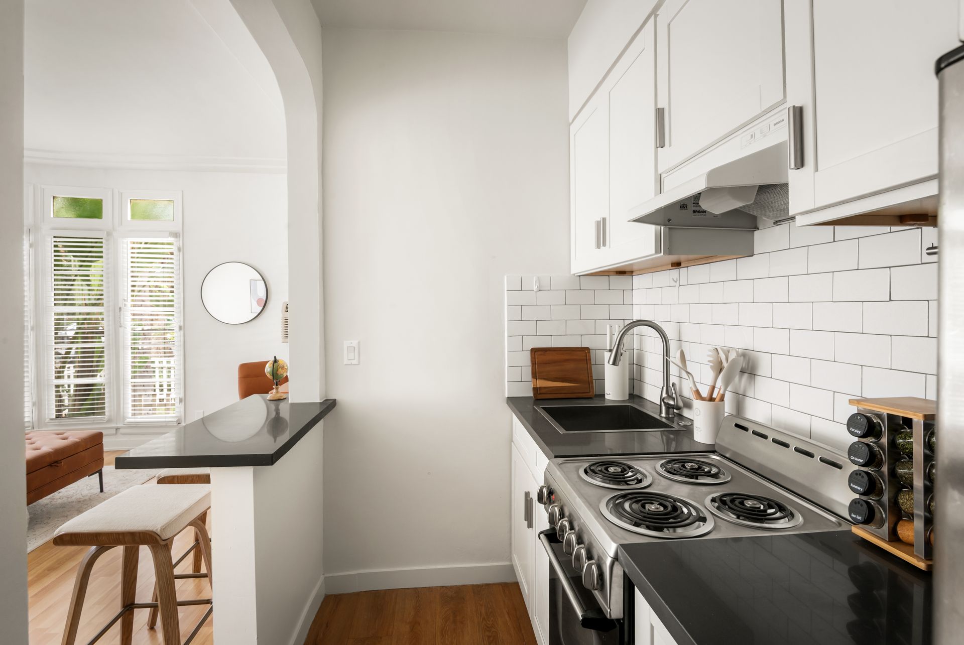 Small white kitchen with a stovetop, black countertops, and a view of a dining area through an archway.