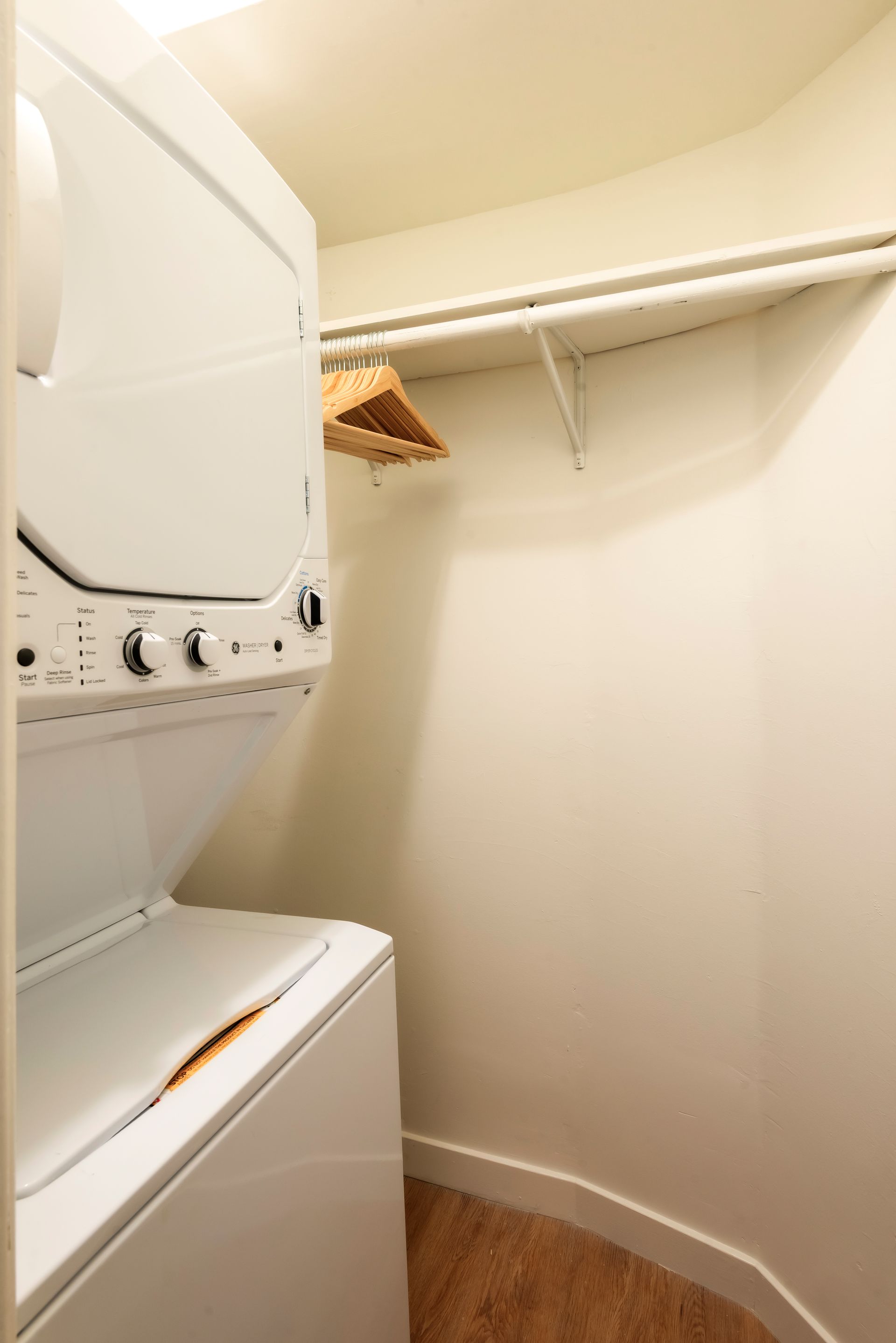 Stacked white washer and dryer in a small laundry closet with a clothes rod and shelf.