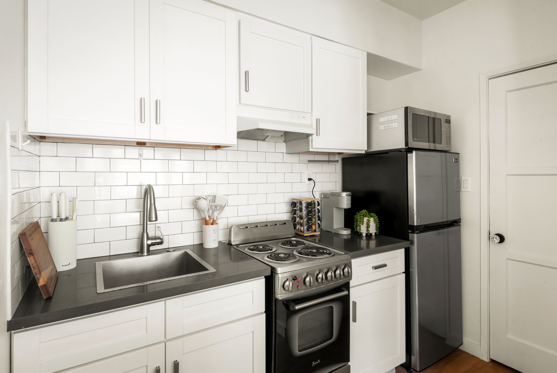 Small, white kitchen with gray countertops, subway tile backsplash, and stainless steel appliances.
