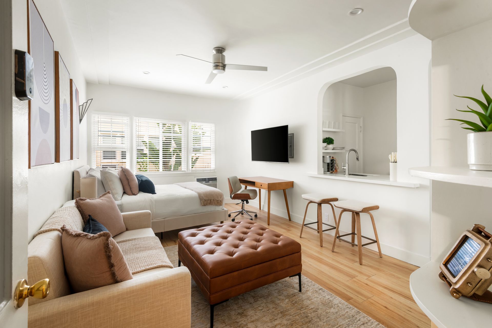 Cozy, bright studio apartment with seating, bed, desk, kitchen pass-through, and TV.