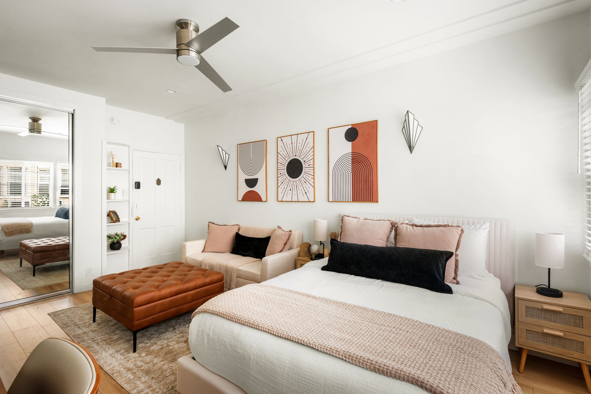 Bedroom with bed, sofa, art, and a ceiling fan, decorated in neutral tones.