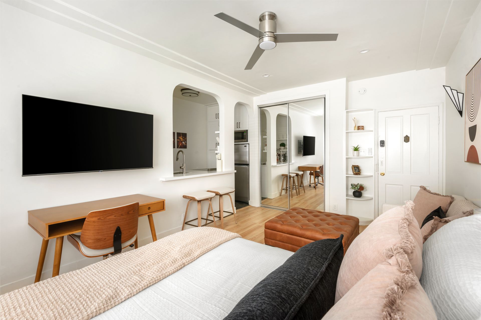 Cozy studio apartment with open kitchen, workspace, and seating area. Bright, white walls, wood floors.