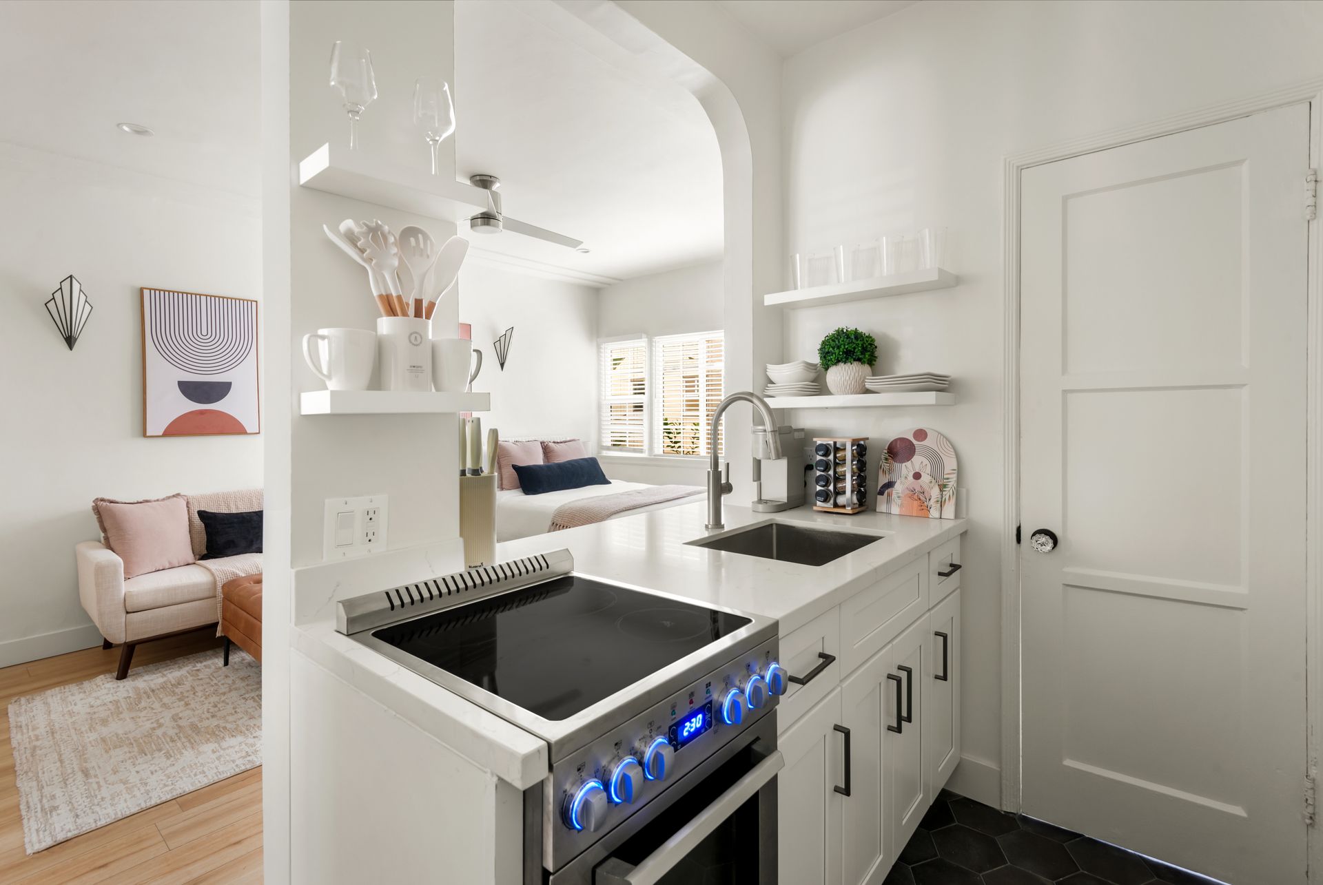 Small white kitchen with a built-in stove, sink, and open archway to a living area with a sofa.