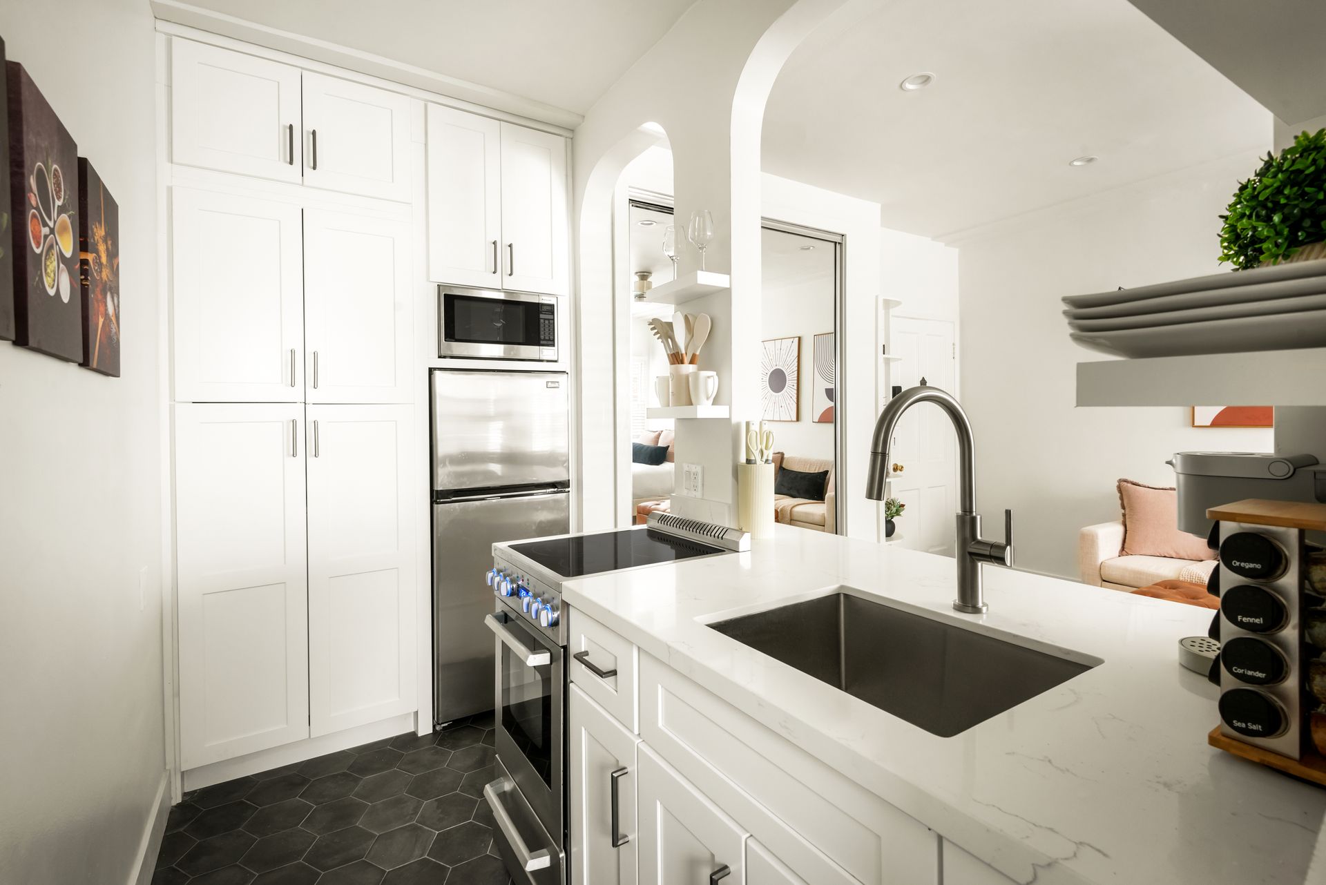 Modern white kitchen with stainless steel appliances, dark sink, and arched doorways.