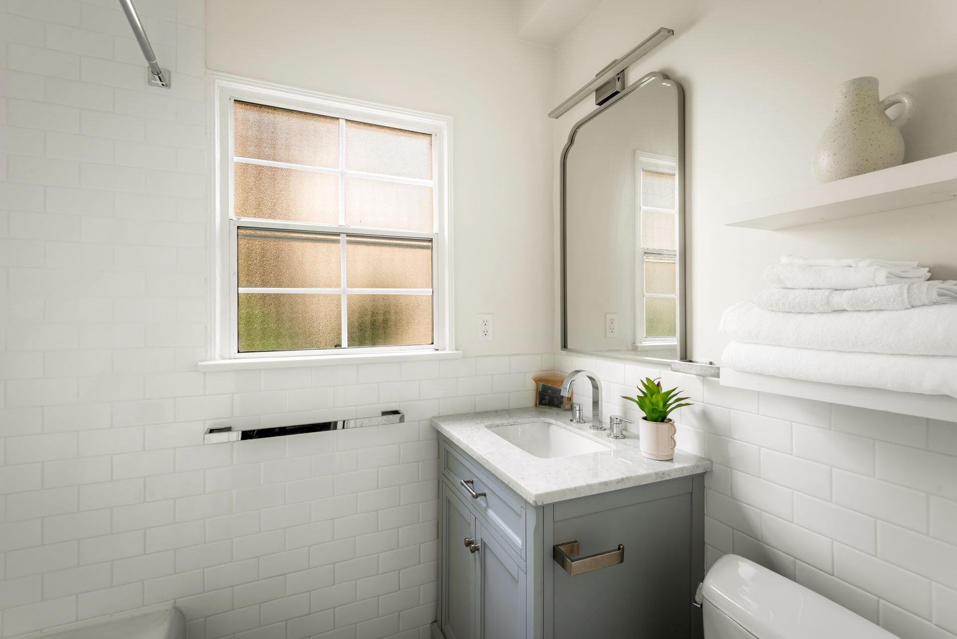 Bathroom with white subway tile, blue vanity, arched mirror, window, and white towels.