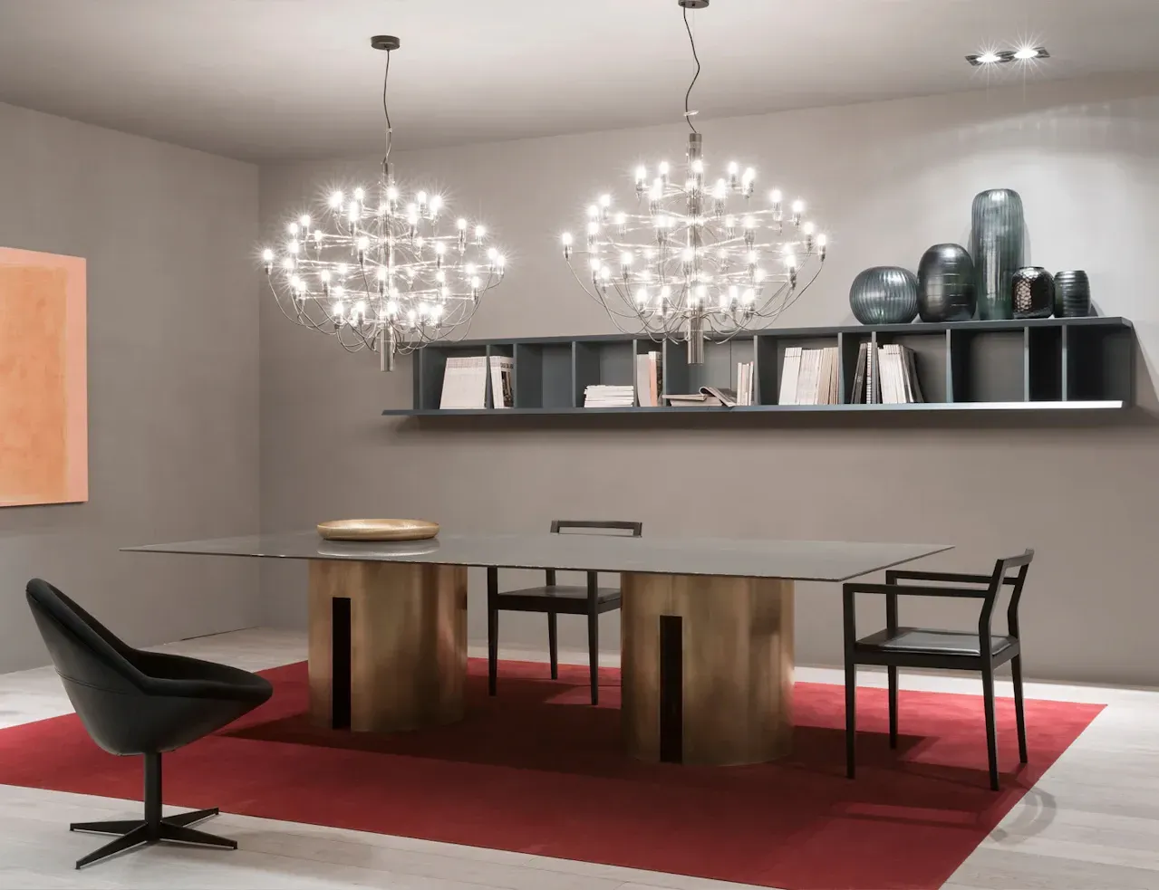 Sala da pranzo con tavolo moderno, sedie e due lampadari. Completano l'arredamento un tappeto rosso e una mensola a muro.