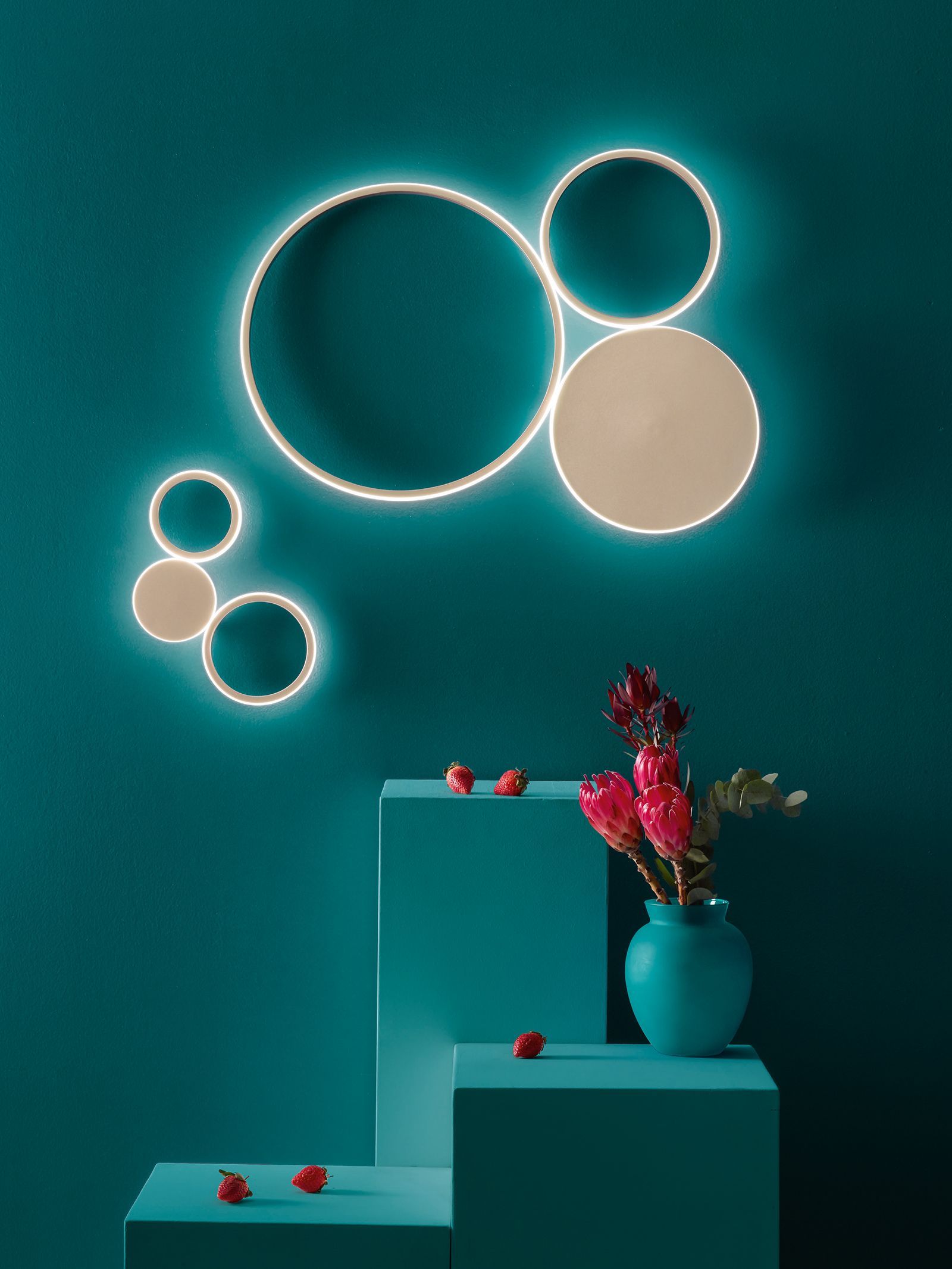 Moderna opera d'arte murale raffigurante cerchi illuminati e vasi di fiori su piedistalli color verde acqua.