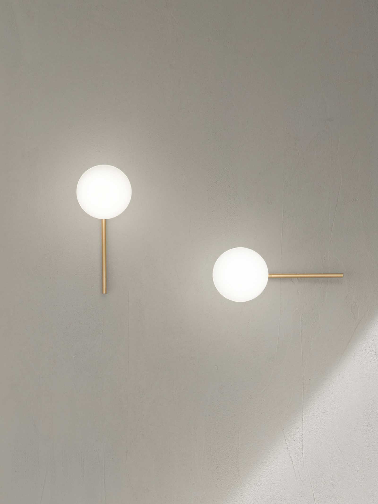 Due applique dorate con sfere bianche luminose su una parete grigia.