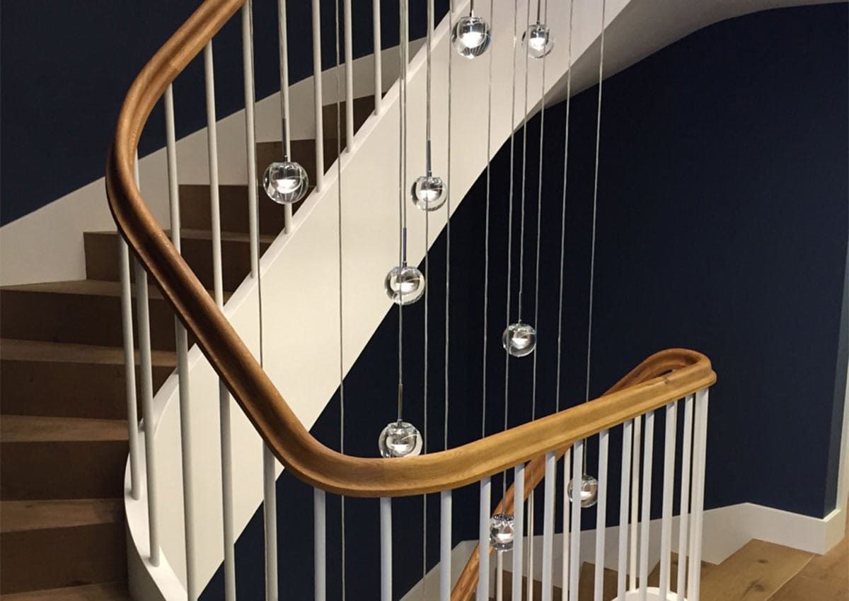 Scala con corrimano in legno, fusi bianchi e luci sferiche sospese contro pareti blu navy.