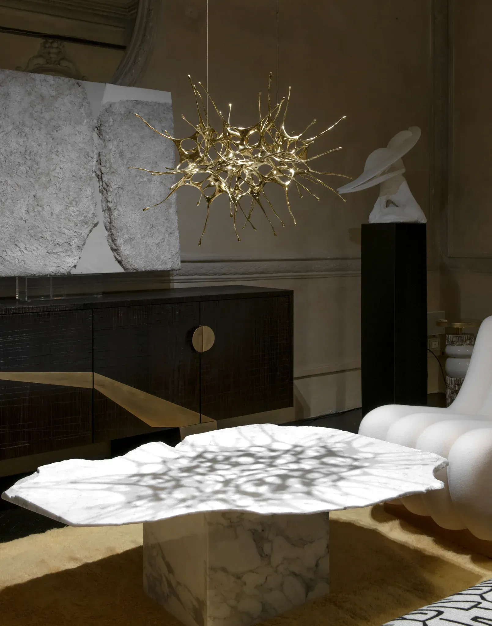 Lussuoso soggiorno con tavolino in marmo, lampadario dorato, opere d'arte ed elementi scultorei bianchi.