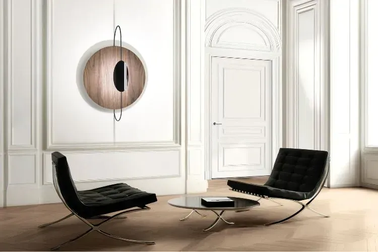 Stanza moderna con sedie nere, una lampada da parete rotonda in legno e un tavolo con piano in vetro.