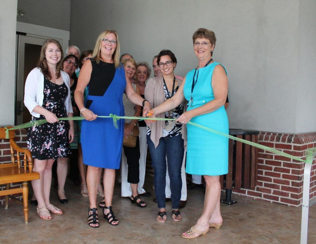 People participating in a ribbon-cutting ceremony in front of a brick building.