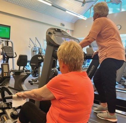 Two people in exercise clothes use treadmills at a brightly lit gym.