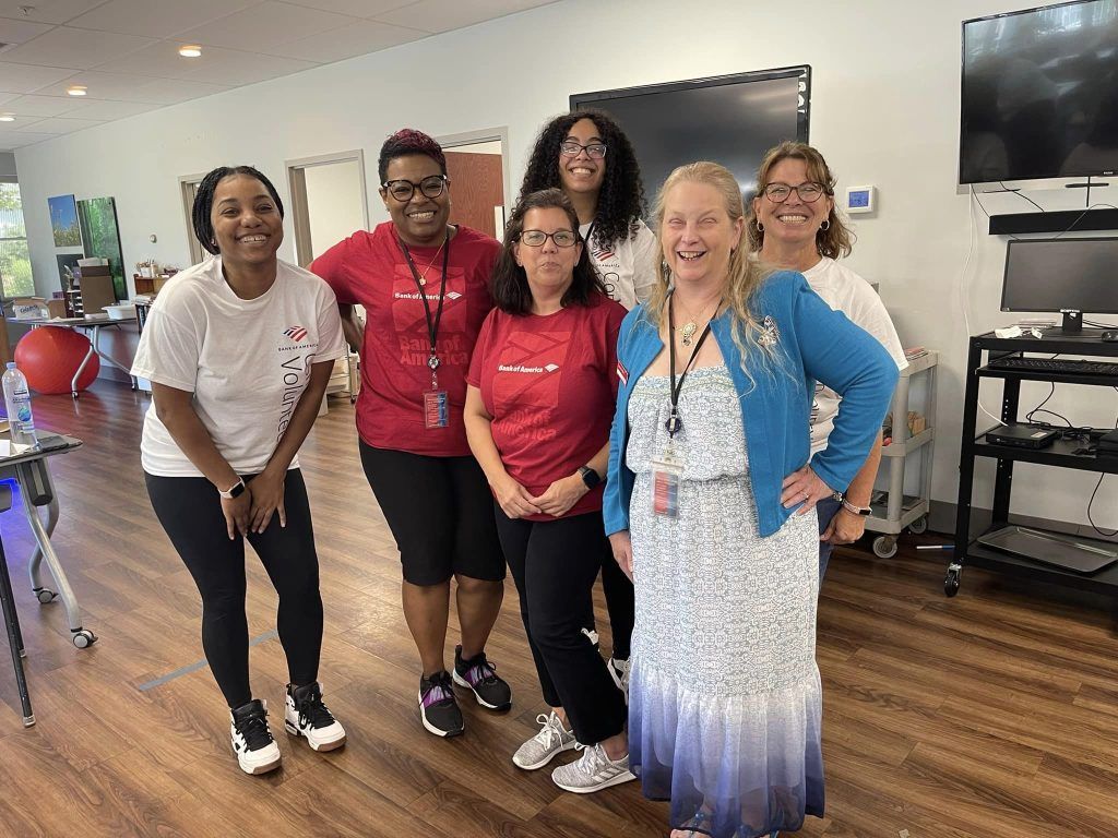 A group of six smiling people stand together in an office setting, posing for a photo.