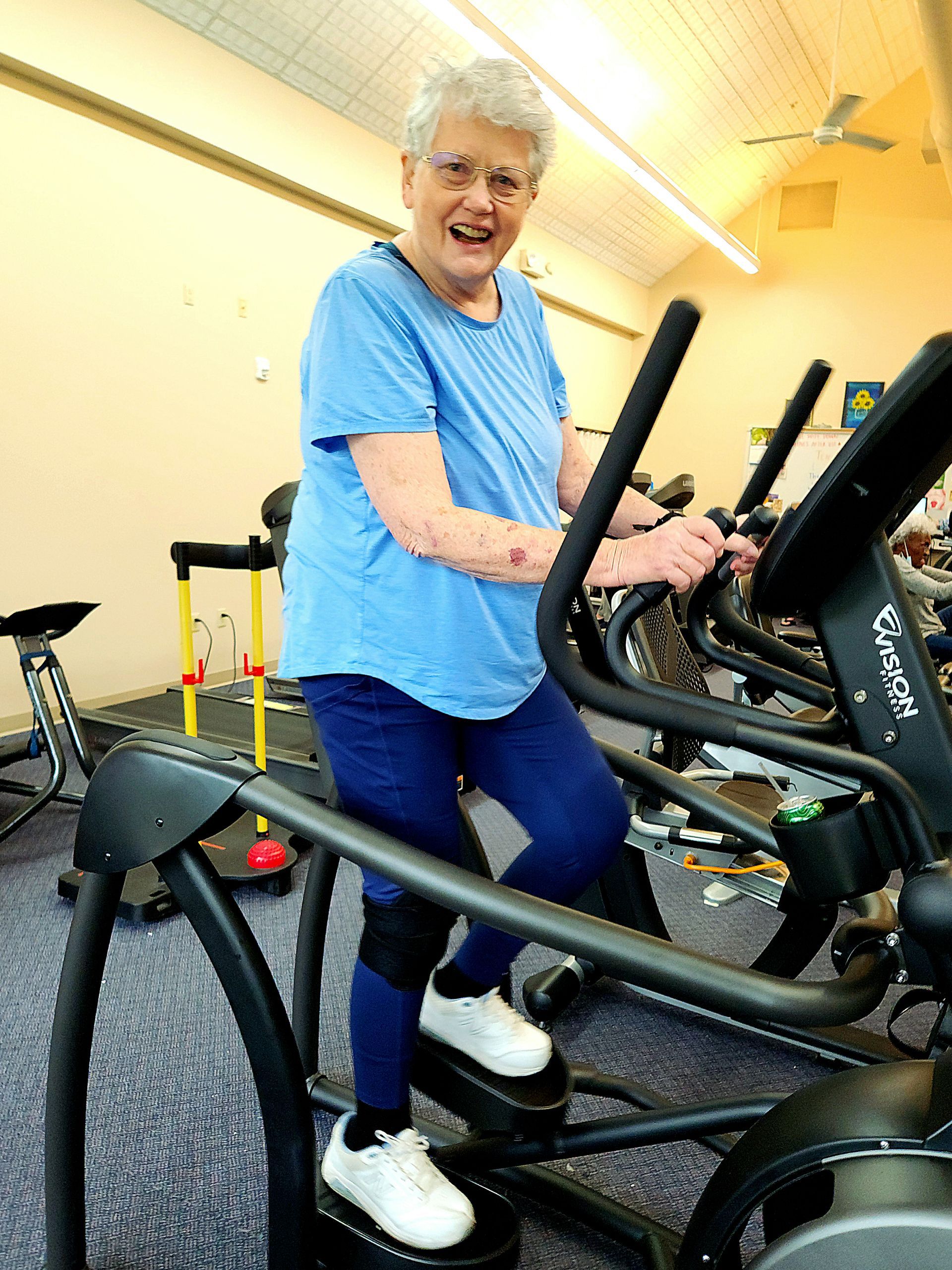 A person smiling while using an elliptical machine in a fitness center.