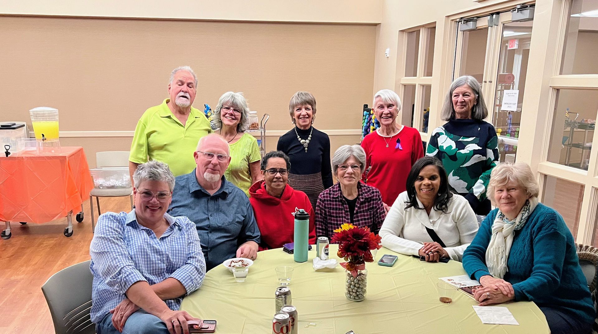 A group of eleven people smiling and posing together around a circular table at an indoor event.