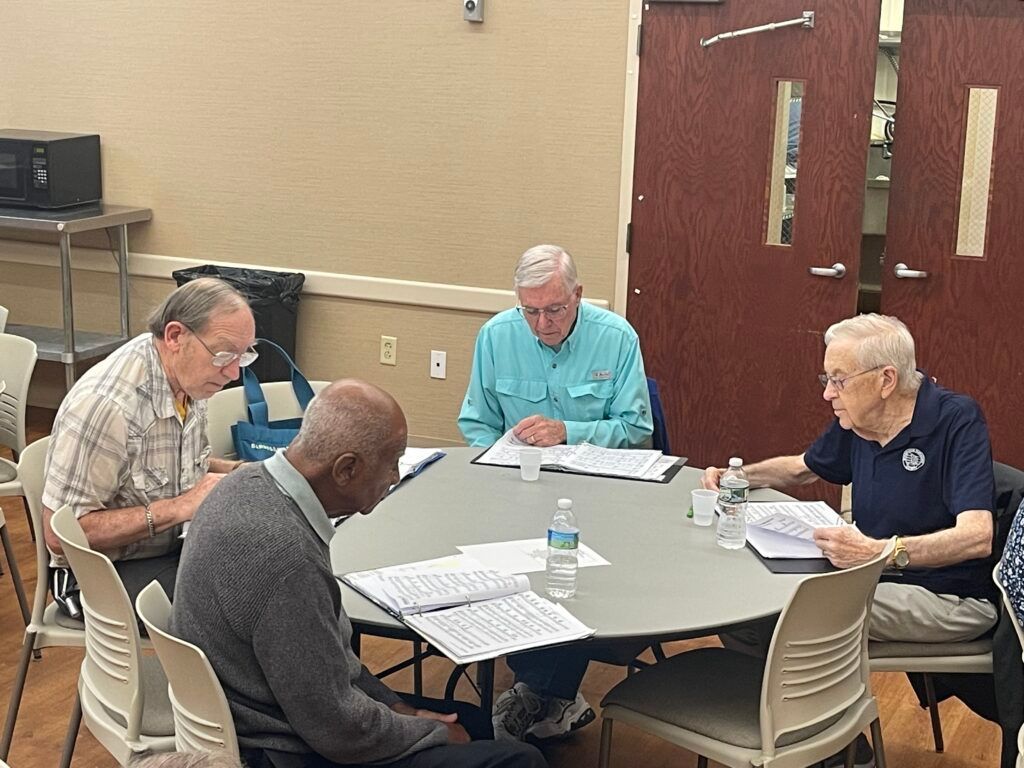 Four people sit around a round table in a meeting room, reading documents and talking.