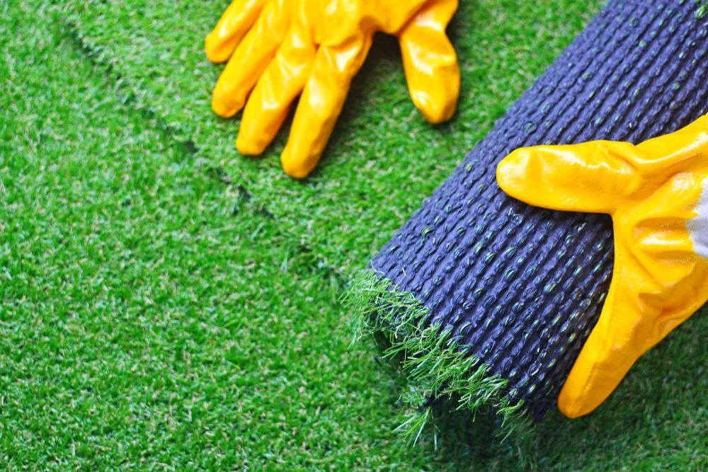 A Person is Holding a Roll of Grass and Wearing Yellow Gloves — Ballina Turf Farm in Wardell, NSW