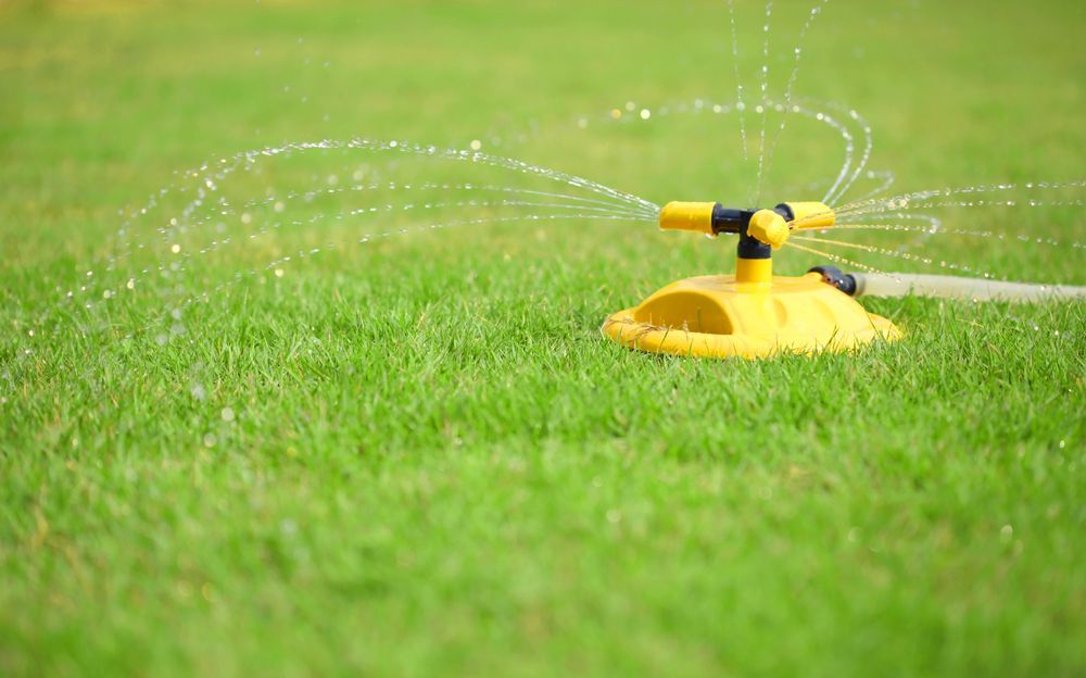 A Yellow Lawn Sprinkler is Spraying Water on a Lush Green Lawn — Ballina Turf Farm in Wardell, NSW