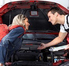 A man and a woman are looking under the hood of a car.