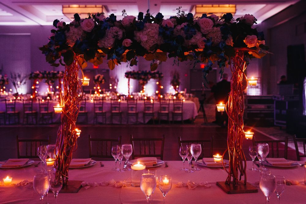 Elegant wedding reception table with a floral arch, warm candlelight, and soft purple lighting in a banquet hall.