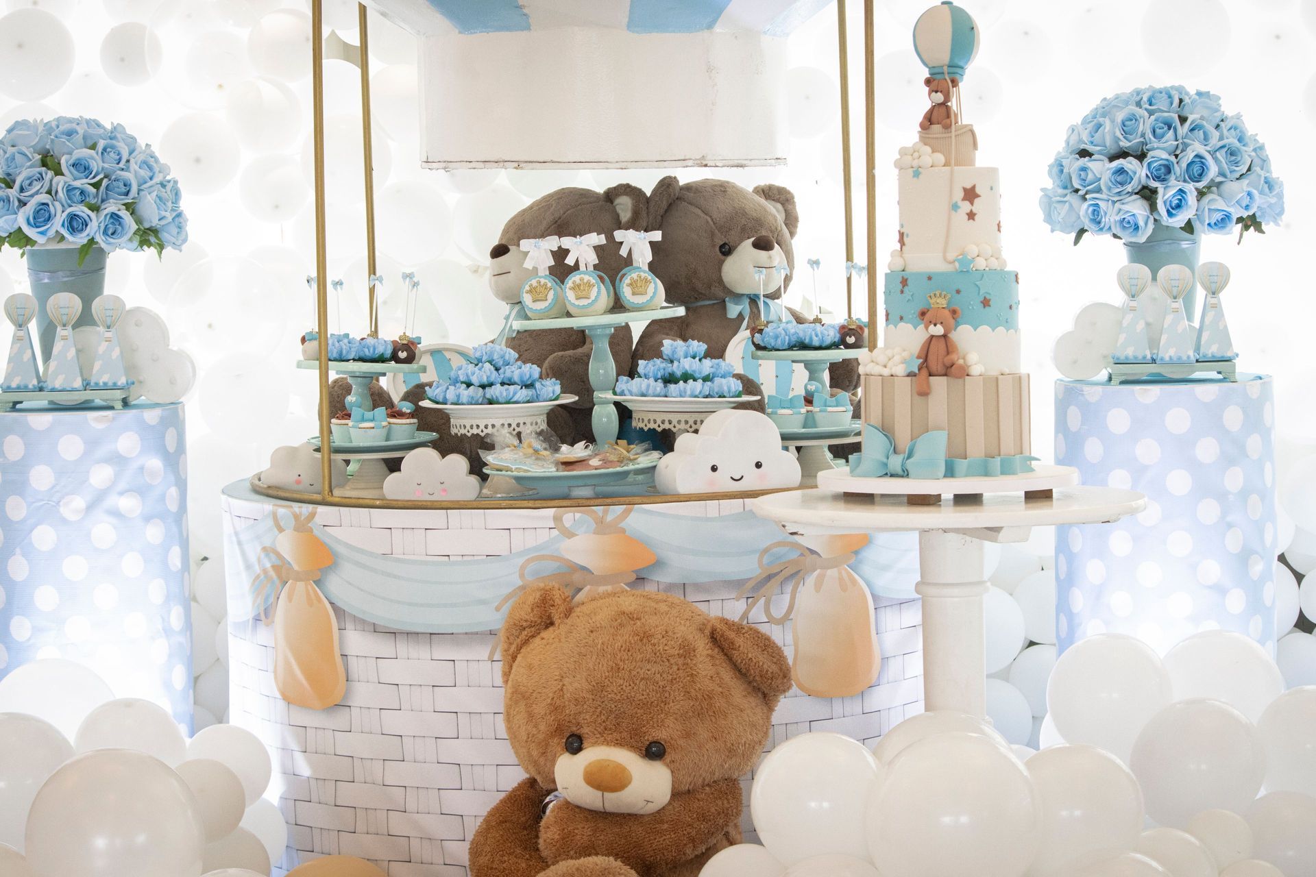 A baby shower display featuring a tiered cake, teddy bears, and blue and white decorations on a table with balloons.