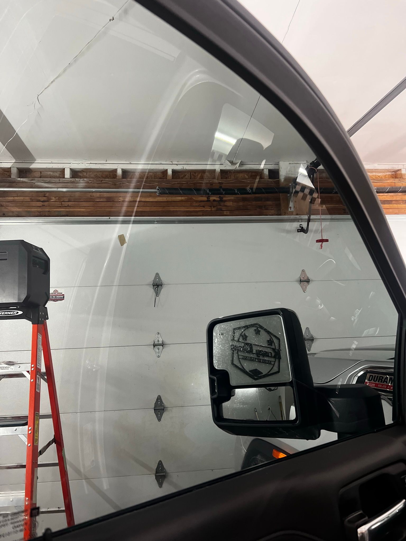 A car is parked in a garage with a ladder in the background.