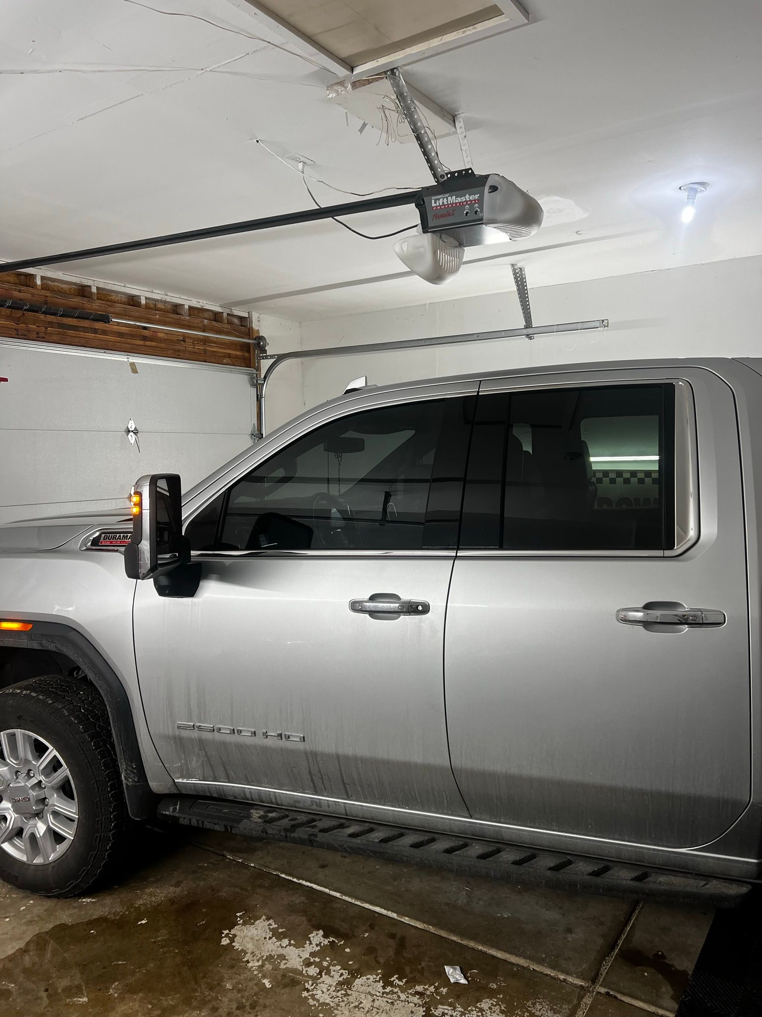 A silver truck is parked in a garage with a garage door open.