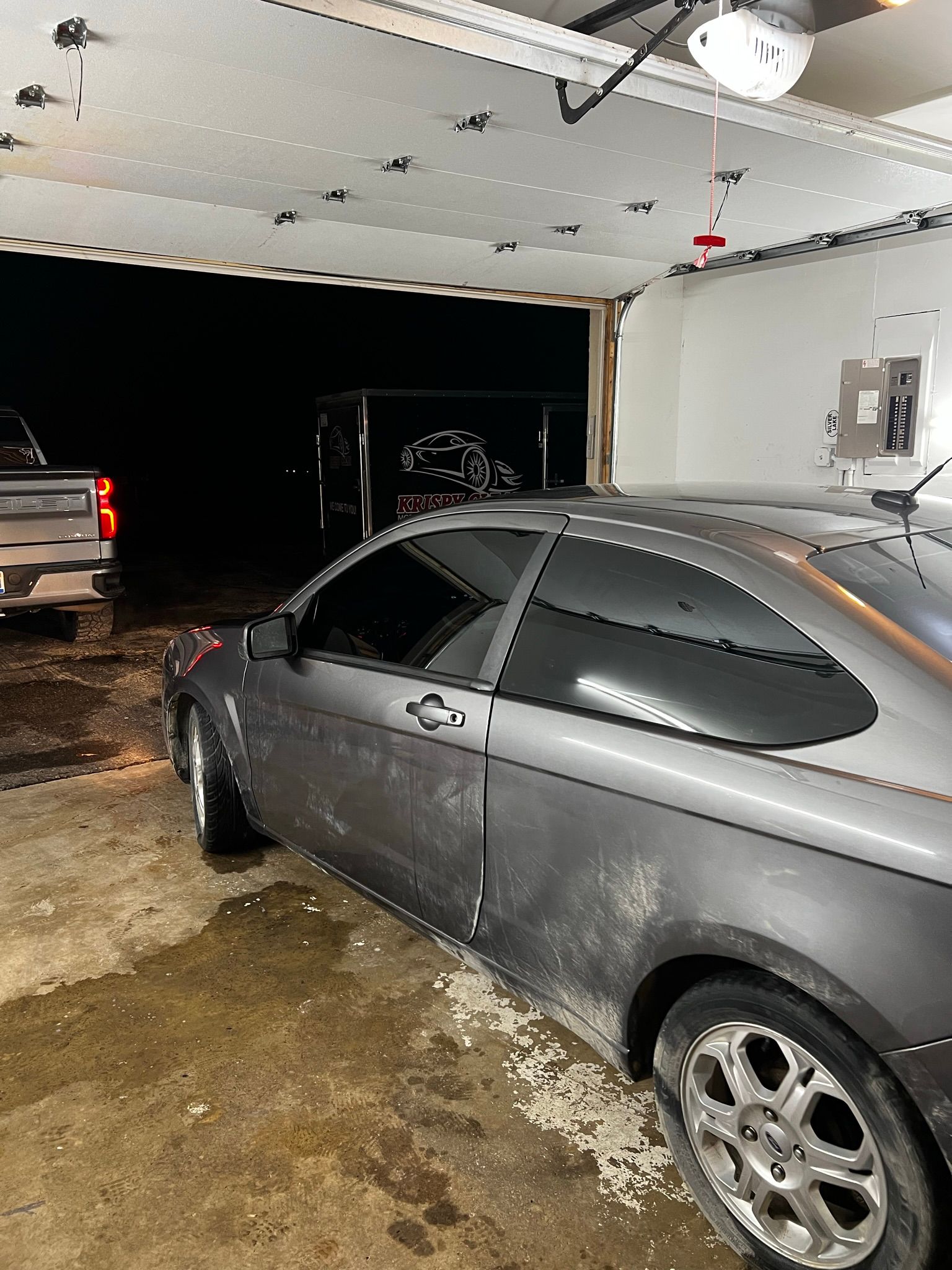 A car is parked in a garage next to a truck.