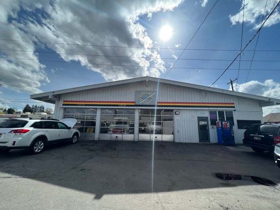 Small white commercial building with parked cars under a bright, cloudy sky