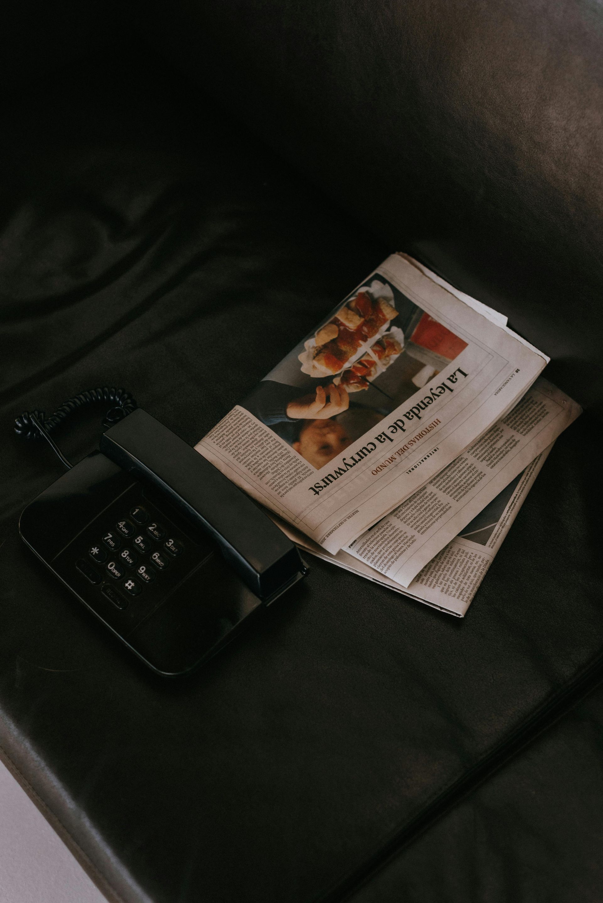 A newspaper and a cell phone are on a table.
