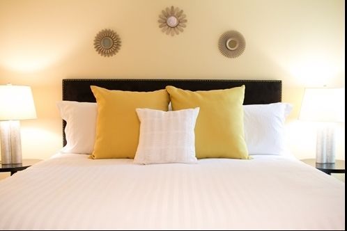Bedroom with white bedding, yellow pillows, and decorative wall art.